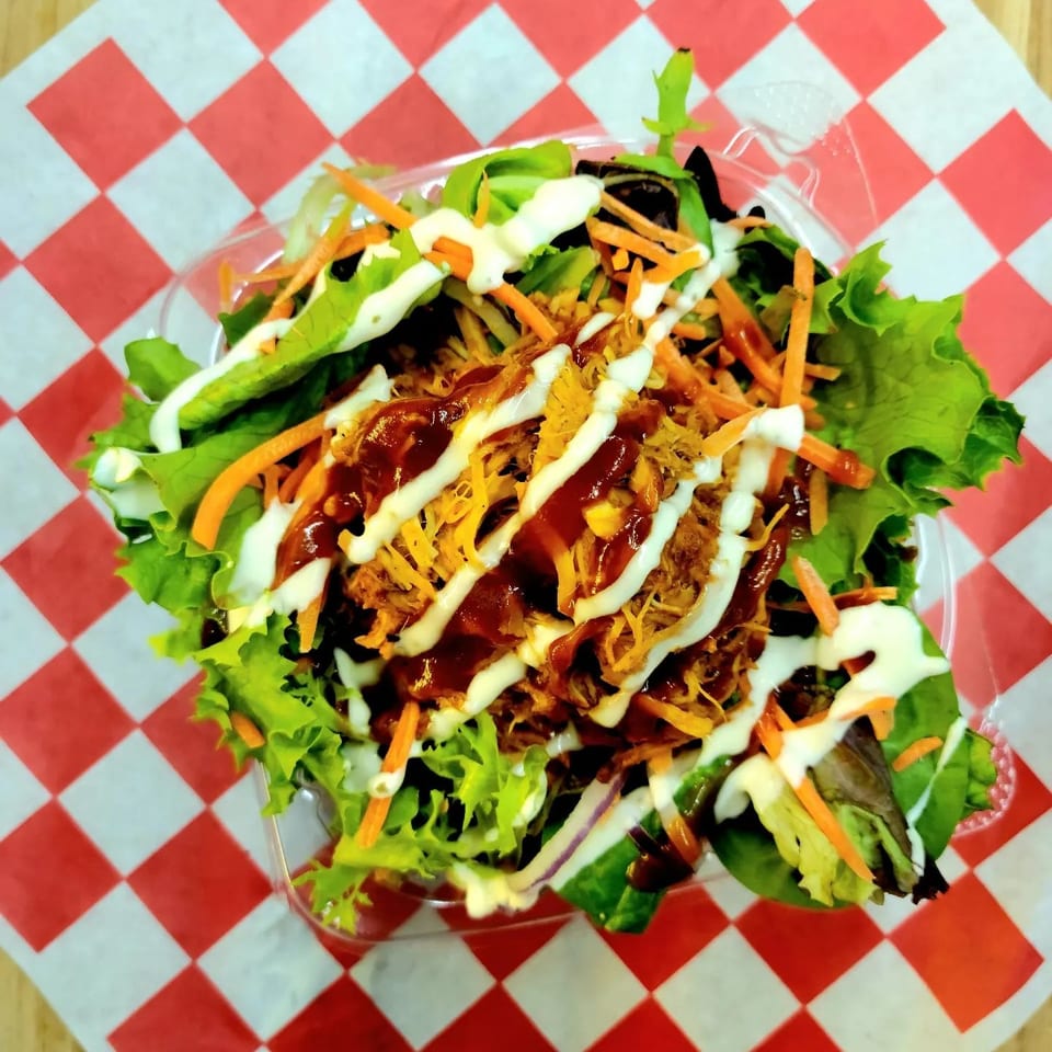 Pulled pork salad with barbecue sauce and ranch dressing on a red and white checkered paper.