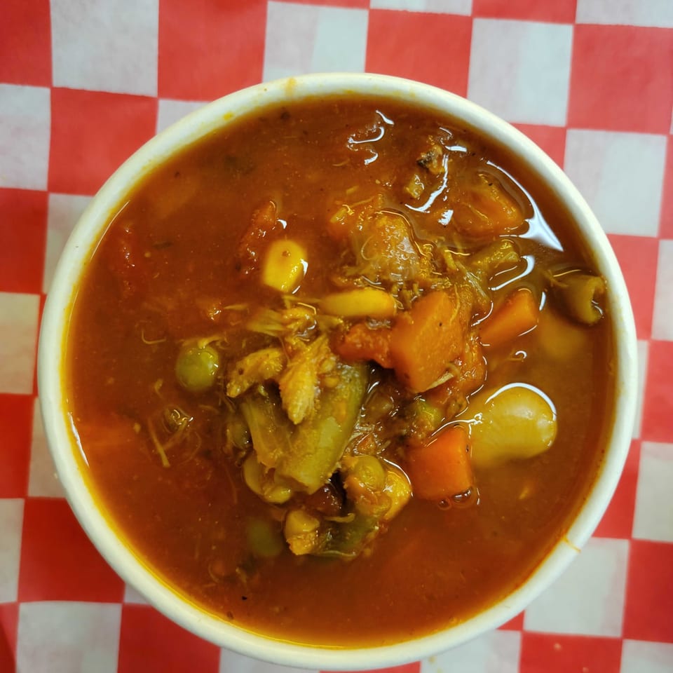 Hearty vegetable and chicken soup in a white bowl on a red and white checkered background.