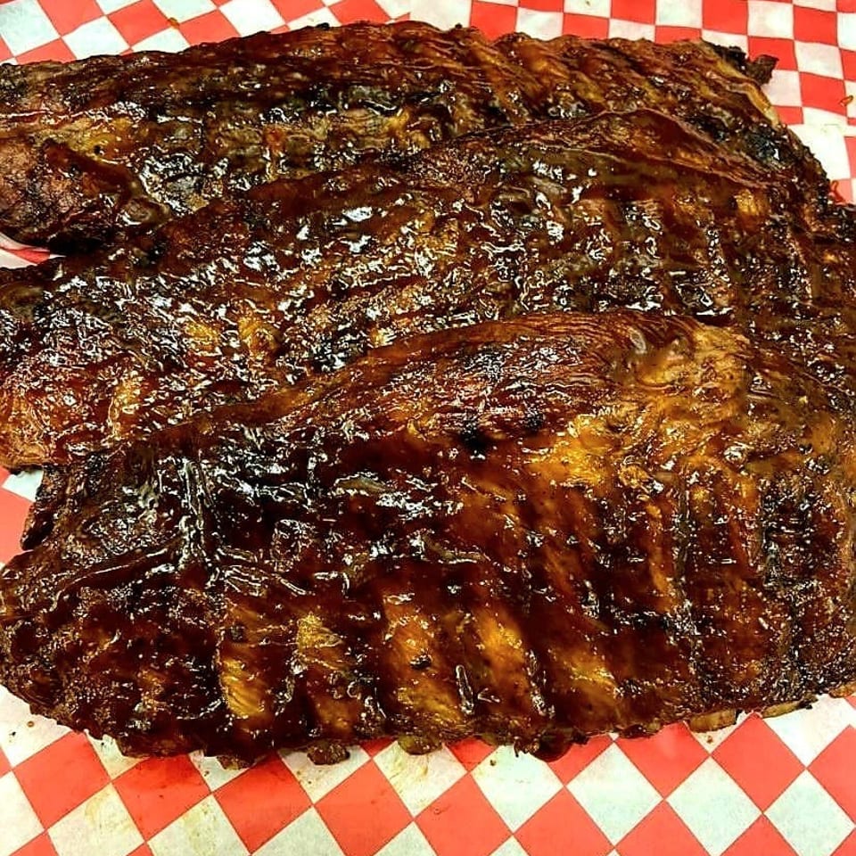 Three racks of glistening, dark brown BBQ ribs on red and white checkered paper.